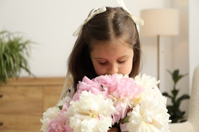 Photo of Cute little girl with bouquet of beautiful peonies at home