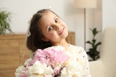 Photo of Cute little girl with bouquet of beautiful peonies at home