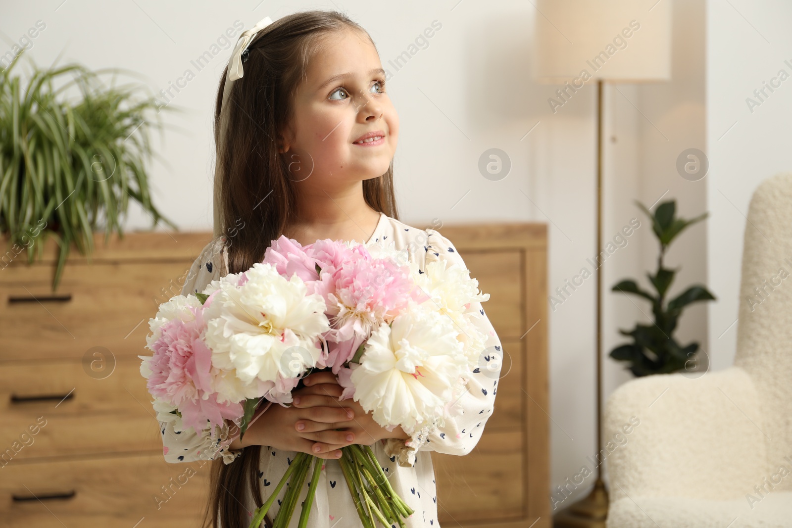 Photo of Cute little girl with bouquet of beautiful peonies at home, space for text