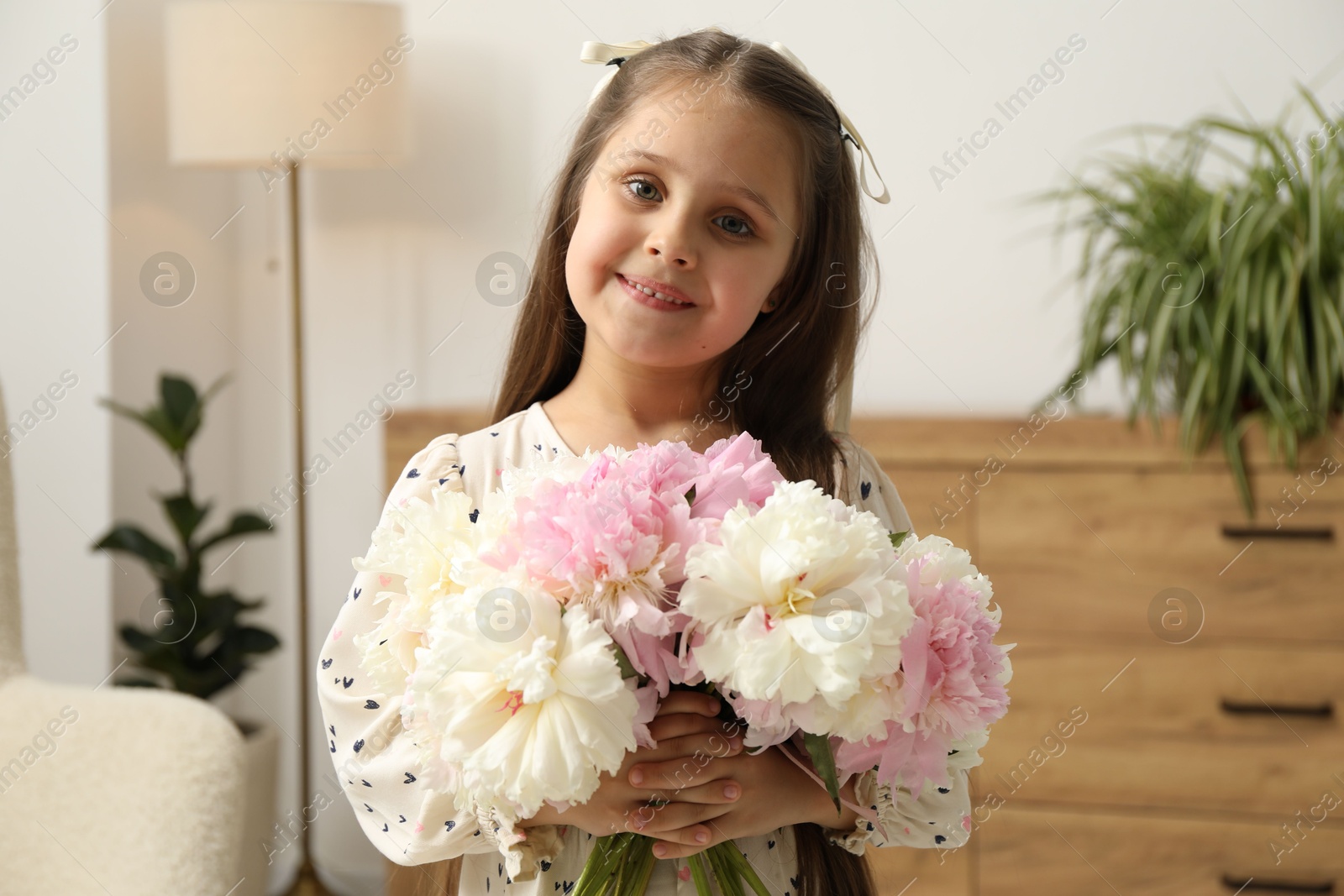 Photo of Cute little girl with bouquet of beautiful peonies at home