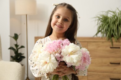 Photo of Cute little girl with bouquet of beautiful peonies at home