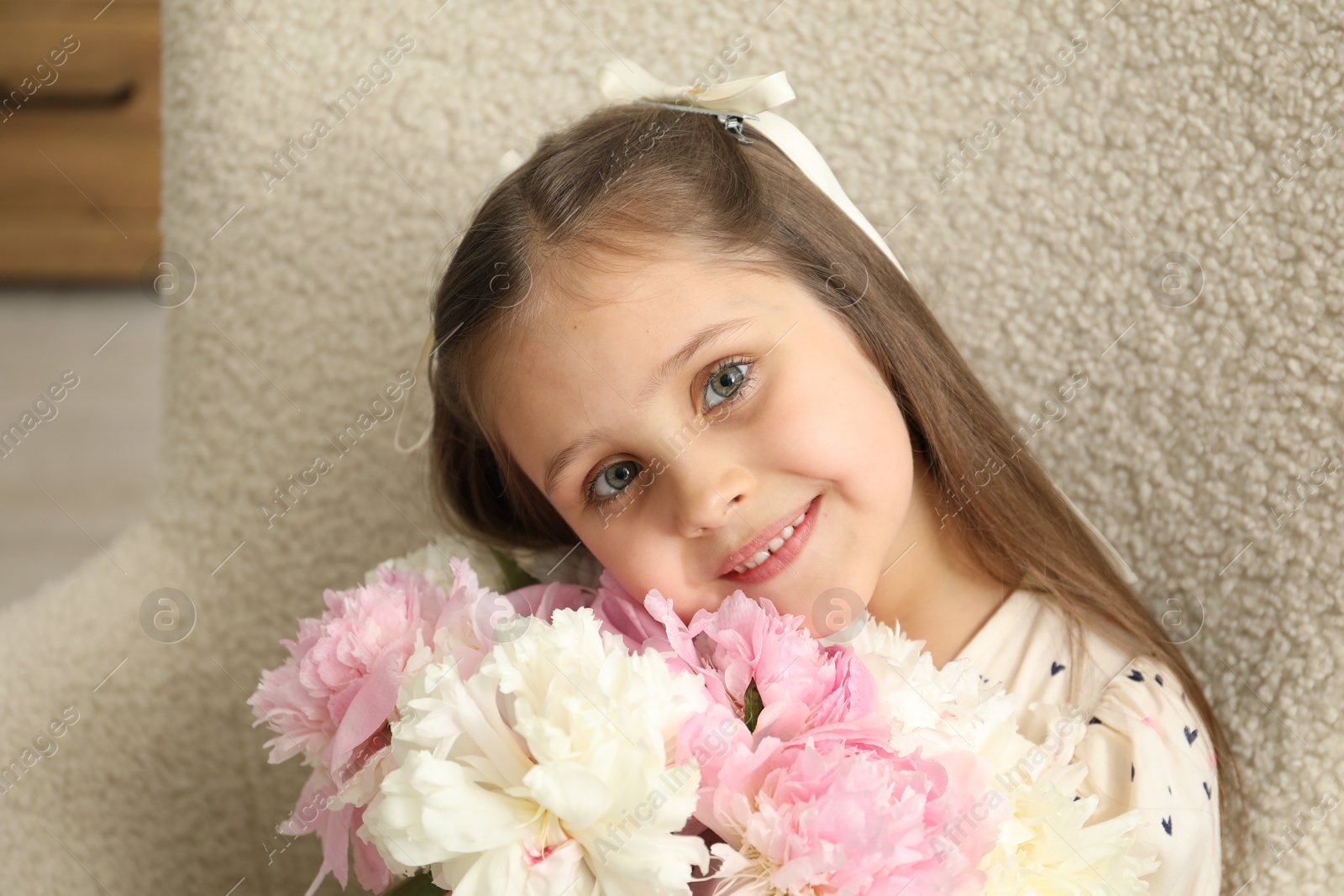 Photo of Cute little girl with bouquet of beautiful peonies in armchair at home