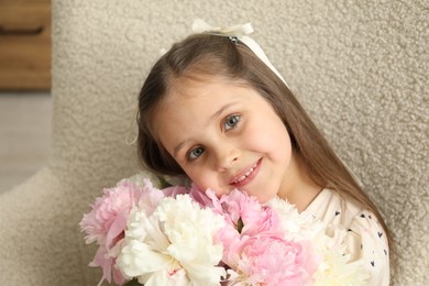 Photo of Cute little girl with bouquet of beautiful peonies in armchair at home