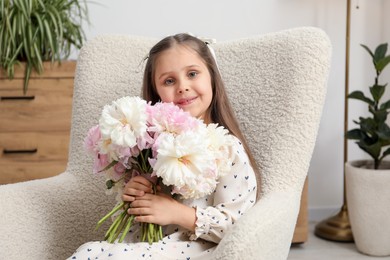 Photo of Cute little girl with bouquet of beautiful peonies in armchair at home