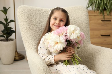 Photo of Cute little girl with bouquet of beautiful peonies in armchair at home