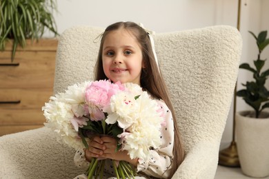 Photo of Cute little girl with bouquet of beautiful peonies in armchair at home