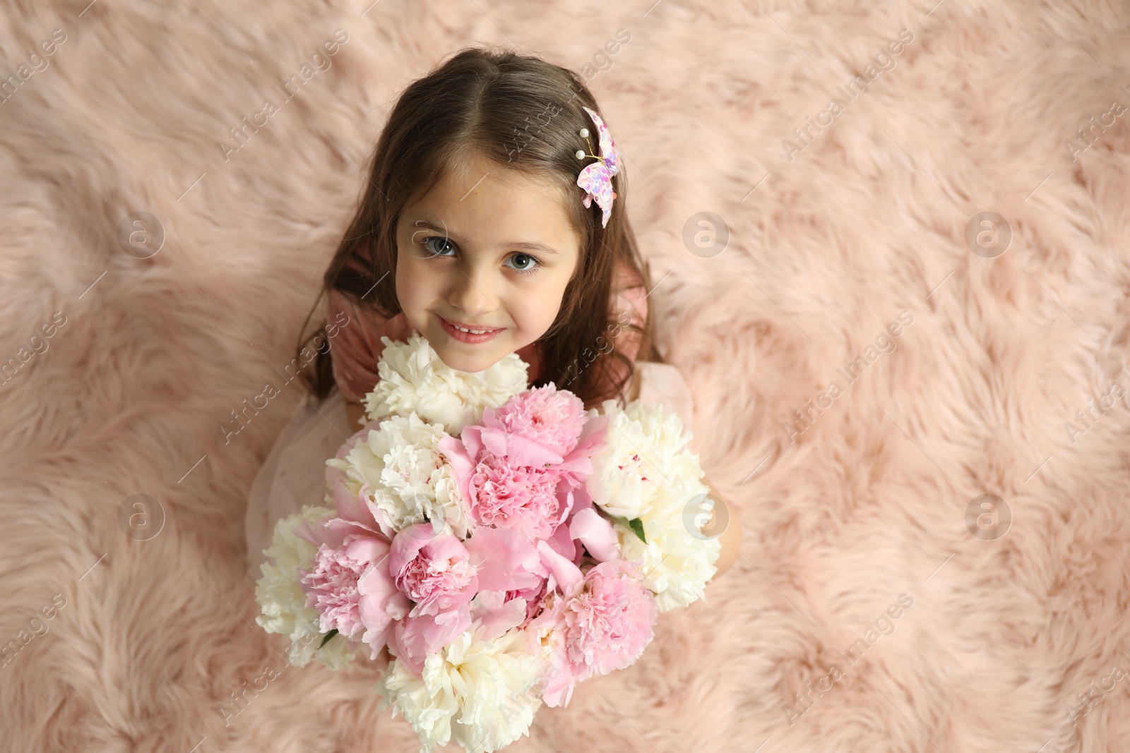 Photo of Cute little girl with bouquet of beautiful peonies on faux fur indoors, above view. Space for text