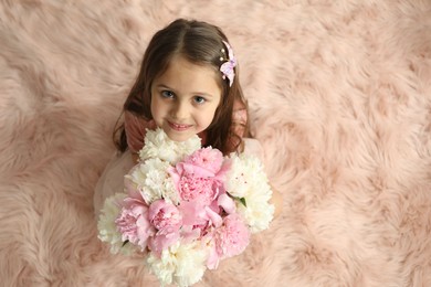 Photo of Cute little girl with bouquet of beautiful peonies on faux fur indoors, above view. Space for text