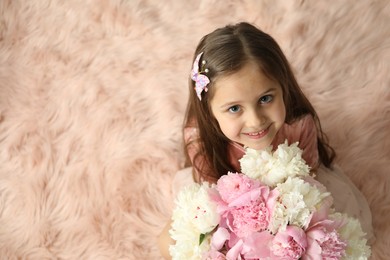 Photo of Cute little girl with bouquet of beautiful peonies on faux fur indoors, above view. Space for text