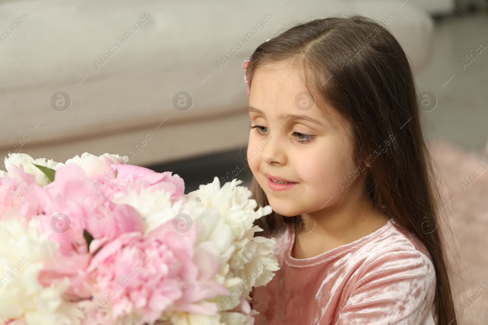 Photo of Cute little girl with bouquet of beautiful peonies at home