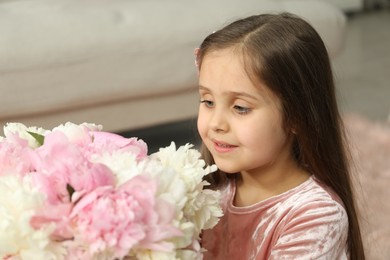 Photo of Cute little girl with bouquet of beautiful peonies at home