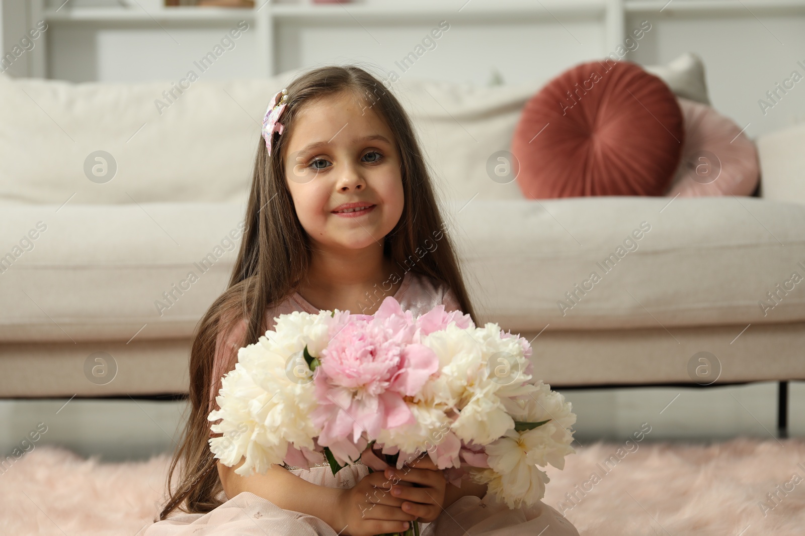 Photo of Cute little girl with bouquet of beautiful peonies on floor at home