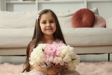 Photo of Cute little girl with bouquet of beautiful peonies on floor at home