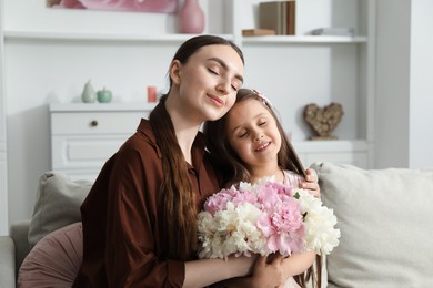 Photo of Mother and her daughter with bouquet of beautiful peonies on sofa at home