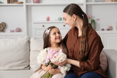Photo of Mother and her daughter with bouquet of beautiful peonies on sofa at home