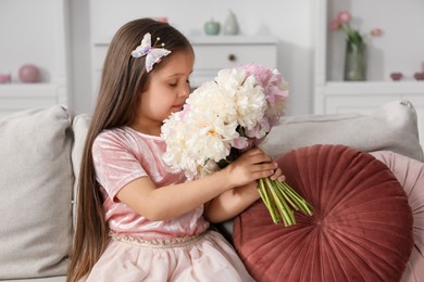 Photo of Cute little girl with bouquet of beautiful peonies on sofa at home