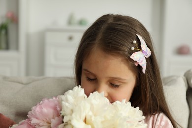 Photo of Cute little girl with bouquet of beautiful peonies at home