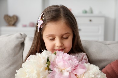 Photo of Cute little girl with bouquet of beautiful peonies at home