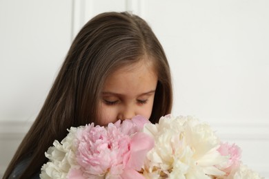 Photo of Cute little girl with bouquet of beautiful peonies near white wall indoors