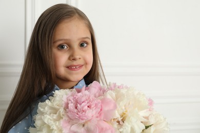 Photo of Cute little girl with bouquet of beautiful peonies near white wall indoors