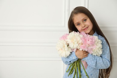 Photo of Cute little girl with bouquet of beautiful peonies near white wall indoors, space for text