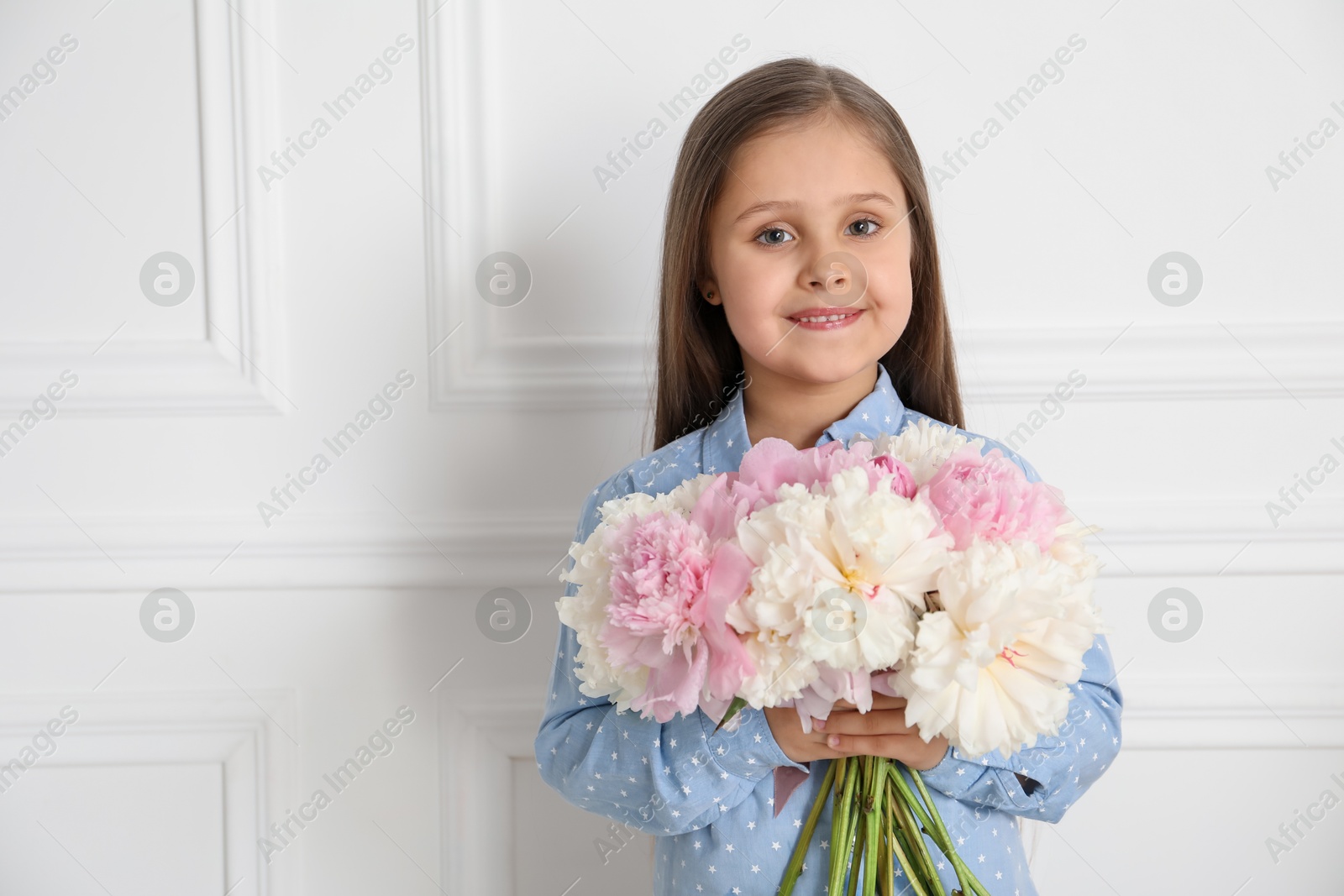 Photo of Cute little girl with bouquet of beautiful peonies near white wall indoors, space for text