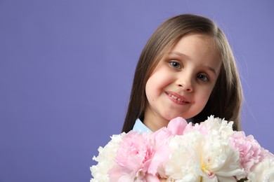 Photo of Cute little girl with bouquet of beautiful peonies on purple background, space for text