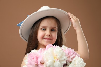 Photo of Cute little girl with bouquet of beautiful peonies on brown background