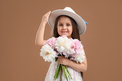 Photo of Cute little girl with bouquet of beautiful peonies on brown background