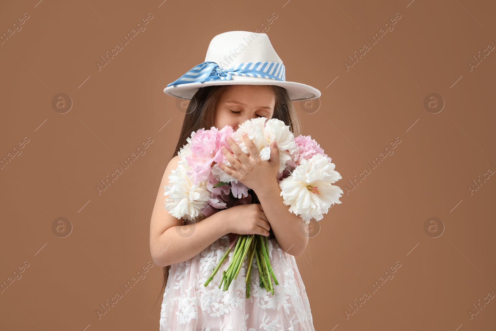 Photo of Cute little girl with bouquet of beautiful peonies on brown background