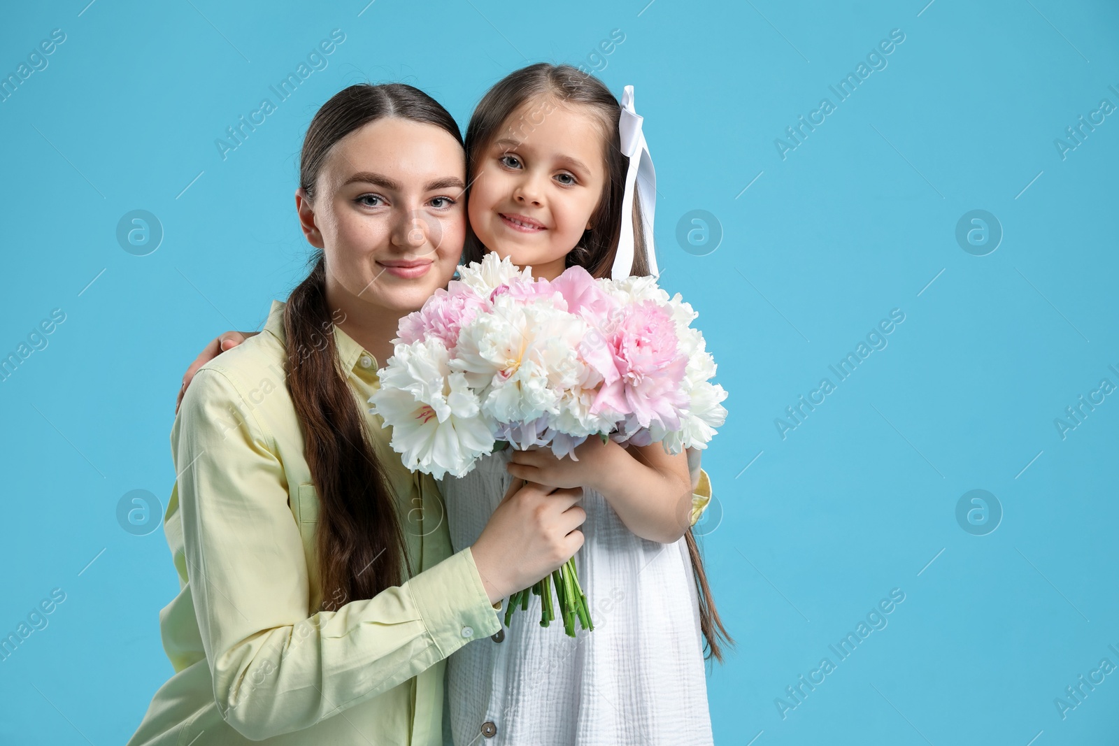 Photo of Mother and her daughter with bouquet of beautiful peonies on light blue background, space for text