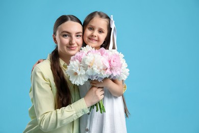 Photo of Mother and her daughter with bouquet of beautiful peonies on light blue background, space for text