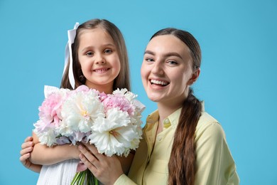 Photo of Mother and her daughter with bouquet of beautiful peonies on light blue background