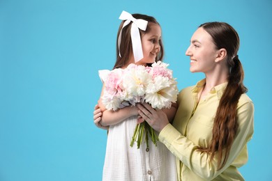 Photo of Mother and her daughter with bouquet of beautiful peonies on light blue background, space for text