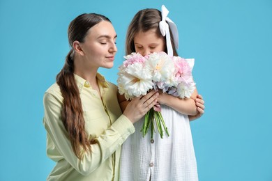 Photo of Mother and her daughter with bouquet of beautiful peonies on light blue background