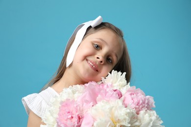Photo of Cute little girl with bouquet of beautiful peonies on light blue background