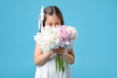 Photo of Cute little girl with bouquet of beautiful peonies on light blue background