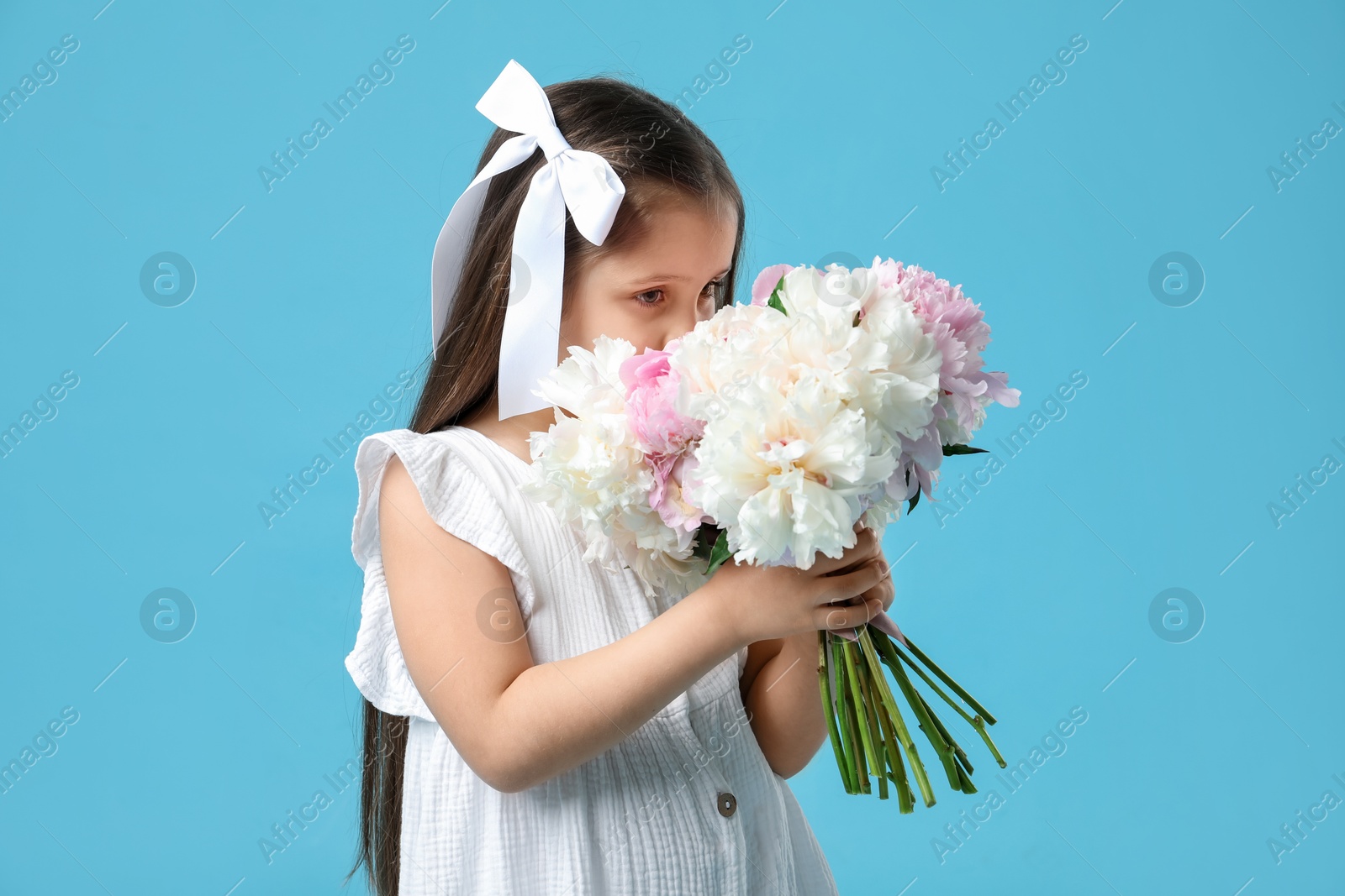 Cute little girl with bouquet of beautiful peonies on light blue background Photo of Cute little girl with bouquet of beautiful peonies on light blue background