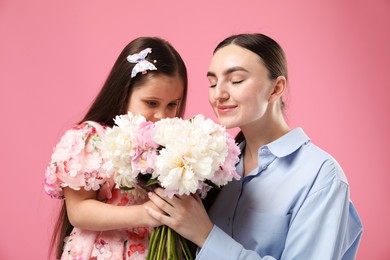 Photo of Cute little girl giving her mother bouquet of beautiful peonies on pink background