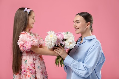 Photo of Cute little girl giving her mother bouquet of beautiful peonies on pink background