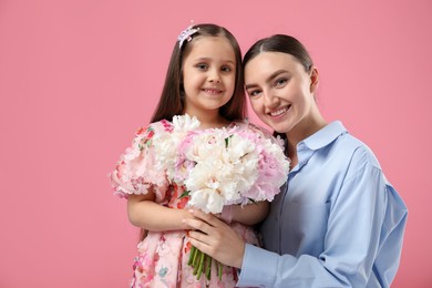 Photo of Mother and her daughter with bouquet of beautiful peonies on pink background
