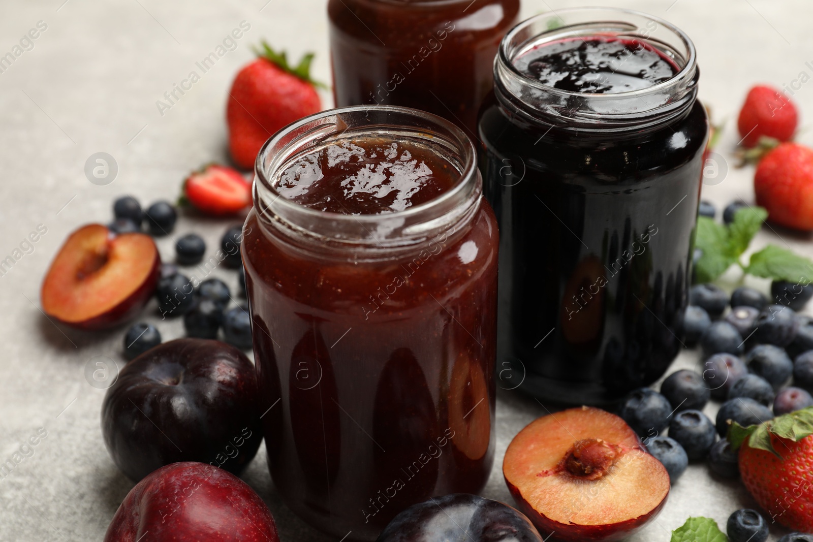 Different sweet jams in jars and ingredients on grey table, closeup Photo of Different sweet jams in jars and ingredients on grey table, closeup