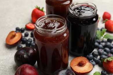 Photo of Different sweet jams in jars and ingredients on grey table, closeup