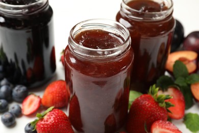 Photo of Different sweet jams in jars and ingredients on table, closeup
