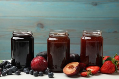 Photo of Different sweet jams in jars and ingredients on white table