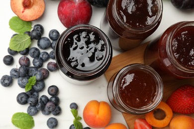 Photo of Different sweet jams in jars and ingredients on white table, flat lay