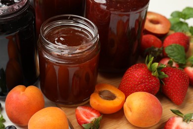 Photo of Different sweet jams in jars and ingredients on table, closeup