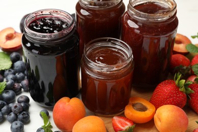 Photo of Different sweet jams in jars and ingredients on table, closeup