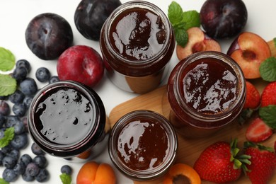 Photo of Different sweet jams in jars and ingredients on white table, flat lay