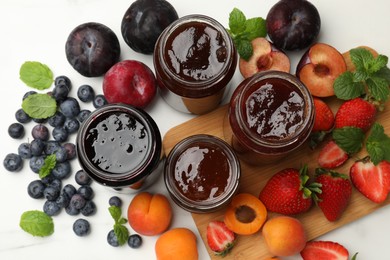 Photo of Different sweet jams in jars and ingredients on white marble table, flat lay